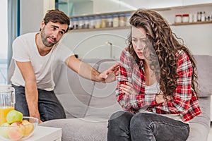 Married couple sitting on gray bed and arguing. Portrait of angry husband screams at crying disappointed wife during a