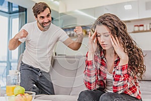 Married couple sitting on gray bed and arguing. Portrait of angry husband screams at crying disappointed wife during a