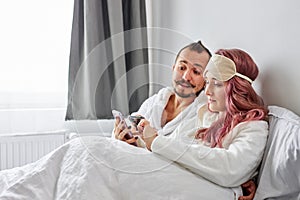 Married couple with smartphones in pajamas on their bed