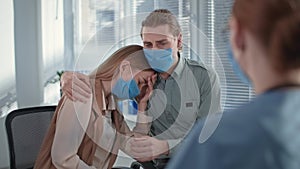 married couple wearing medical masks receive negative news during doctor consultation in hospital office