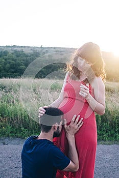 A married couple who are expecting a baby are photographed at sunset in a flower field. A pregnant woman and her loving man. The