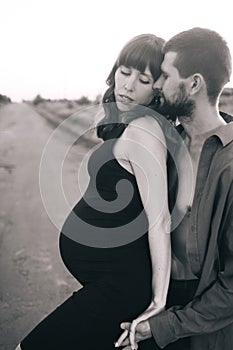 A married couple who are expecting a baby are photographed at sunset in a flower field. A pregnant woman and her loving man. The