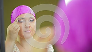 A married Jewess in front of a mirror does eye makeup with violet shadows with a brush