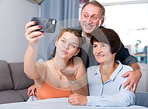 Marrieds with their adult daughter are takinf selfie together on sofa photo