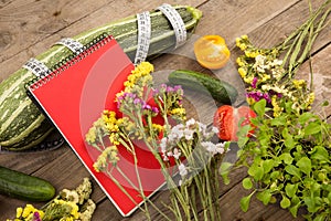 marrow squash, measure tape, blank red notepad, flowers, tomatoes and cucumbers on brown wooden table