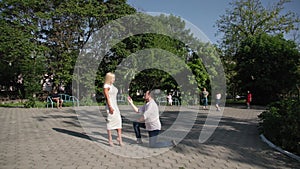 marry me, romantic man kneels with ring in box in his hands and proposes to charming woman in park background of trees