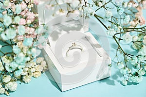 Marry me. White gift box with engagement diamond ring and fresh spring flowers on blue background