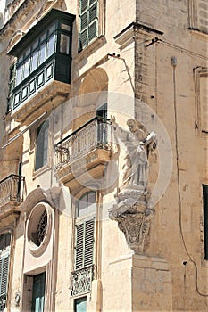 Marsaskala, Malta, July 2016. Statue of a saint with a book on the corner of a residential Maltese house in a small town.