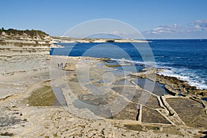 MARSAXLOKK, MALTA - 03 JAN, 2020: Traditional salt fields, Mediterranean Sea and small limestone hill in the background