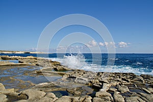 MARSAXLOKK, MALTA - 03 JAN, 2020: Traditional salt fields, Mediterranean Sea and small limestone hill in the background