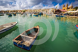 Marsaxlokk, Malta - Traditional colorful maltese Luzzu fisherboats at the old market of Marsaxlokk with green sea water, blue sky