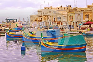 A number of colourful traditional Maltese fishing boat Luzzu docking with old houses behind at fishing village Marsaxlokk, Malta