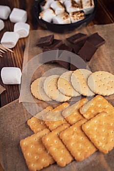 marshmallows, chocolate and cookies for making smore on brown background. view from above. copy space