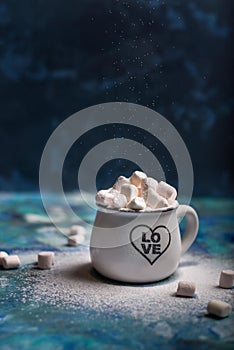 Marshmallows in cocoa in white mug with scattered mini marshmallows on blue  background