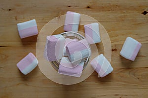 Marshmallows colorful white and pink in glass cup isolated on wooden background. Sweet candy dessert.