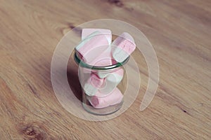 Marshmallows colorful white and pink in glass cup isolated on wooden background. Sweet candy dessert.