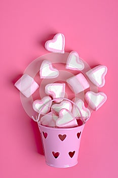 Marshmallows and heart shaped candies spilled from a pink iron bucketon a pink background Happy Valentine`s Day