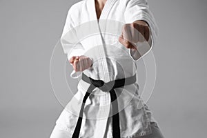 Martial arts master in keikogi with black belt against grey background, focus on fist