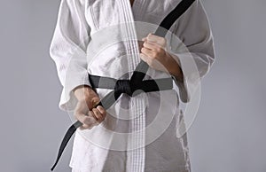 Martial arts master in keikogi with black belt on grey background, closeup