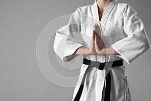 Martial arts master in keikogi with black belt on grey background, closeup. Space for text