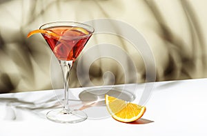 Martinez alcoholic cocktail drink with red vermouth, liqueur, orange bitter, zest and ice. Light beige background, hard light,