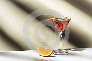 Martinez alcoholic cocktail drink with red vermouth, liqueur, orange bitter, zest and ice. Light beige background, hard light,