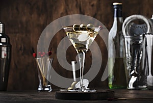 Martini cocktail, with dry vermouth, vodka and green olives, vintage wood bar counter with bar tools