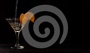 A Martini glass on a black background. cocktail with oranges. Martinis are poured. horizontal banner for designers
