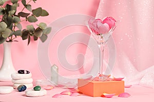 Martini glass with flowers, stones and petals on pink background