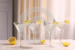Martini glasses with fresh cocktail, rosemary and lemon on white table indoors