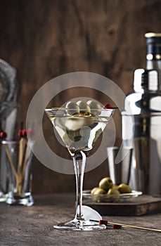 Martini vodka cocktail, with dry vermouth, vodka and green olives, bar tools, vintage wood counter, selective focus