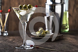 Martini vodka cocktail, with dry vermouth, vodka and green olives, bar tools, vintage wood counter, selective focus