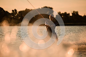 marvelous view of attractive man holding rope and energetically riding wakeboard on splashing river wave.