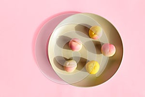 Marzipan fruits in the plate on pink pastel background. Martorana fruit molded a shape of peaches. Typical sicilian pastries -