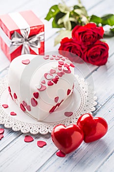 Marzipan white cake in the shape of a heart with red hearts. As the decoration bouquet of red roses a gift from the ribbon.