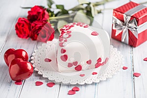 Marzipan white cake in the shape of a heart with red hearts. As the decoration bouquet of red roses a gift from the ribbon.