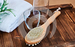 Masage brush, body skin care and coffee natural scrub in glass, white towel and greens on dark wooden background. photo