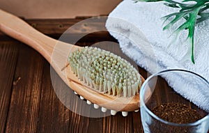Masage brush, body skin care and coffee natural scrub in glass, white towel and greens on dark wooden background.