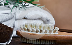 Masage brush, body skin care and coffee natural scrub in glass, white towel and greens on dark wooden background.