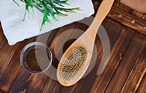 Masage brush, body skin care and coffee natural scrub in glass, white towel and greens on dark wooden background. photo