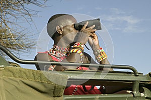 Masai scout with binoculars looks for animals from a Landcruiser during a tourist game drive at the Lewa Wildlife Conservancy in