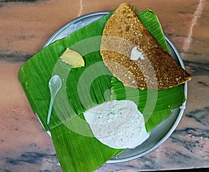 Masala dosa and coconut chutney served on banana leaves alongwith badam pudding photo