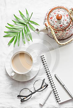 Masala tea, teapot, notepad, glasses, pen, green flower leaf on white background, top view. Morning inspiration planning.