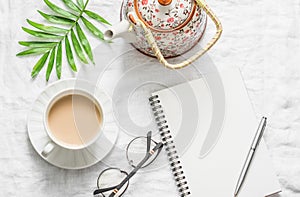 Masala tea, teapot, notepad, glasses, pen, green flower leaf on white background, top view. Morning inspiration planning.