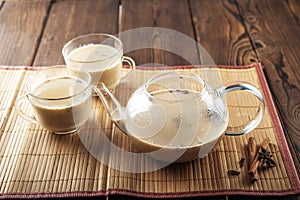 Masala tea on a textural wooden background. A teapot is a transparent tea pot with mugs and Indian national tea masala. Milk, ging photo