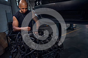 Masculine African American auto-mechanic standing near big black engine