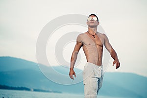 Masculine body man in sunglasses at beach with mountauns on background