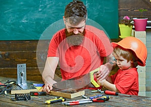 Masculine duties concept. Father, parent with beard teaching little son to sawing with sharp handsaw, carpenter crafts