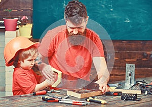 Masculine duties concept. Father, parent with beard teaching little son to sawing with sharp handsaw, carpenter crafts