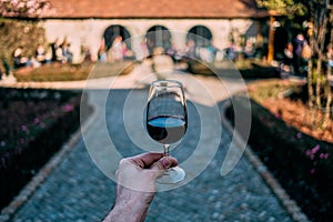 Masculine hand holding glass of Port Wine with winery and garden on the background, in Porto Portugal, city of the Port Wine